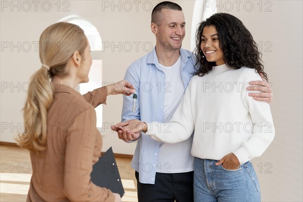 Female realtor handing smiley couple keys their new home