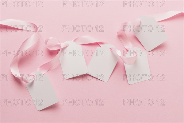 Overhead view blank tags pink ribbon against plain pink backdrop