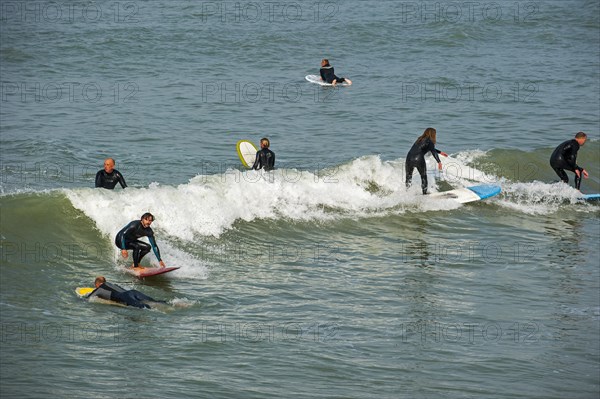 Surfers in wetsuits riding wave on surfboards as it breaks at sea