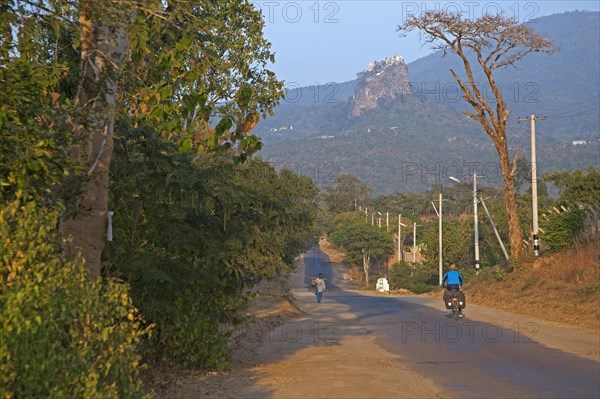 Tourist cycling towards Buddhist monastery on the summit of Taung Kalat near the volcano Mount Popa