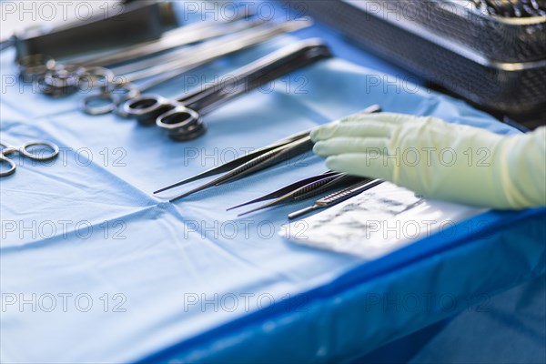 A hand reaches for a pair of tweezers in an operating theatre