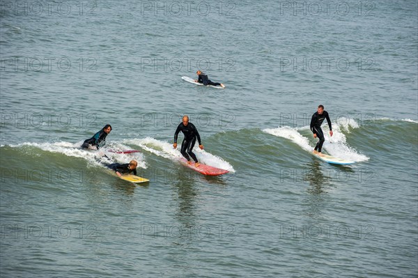 Surfers in wetsuits riding wave on surfboards as it breaks at sea