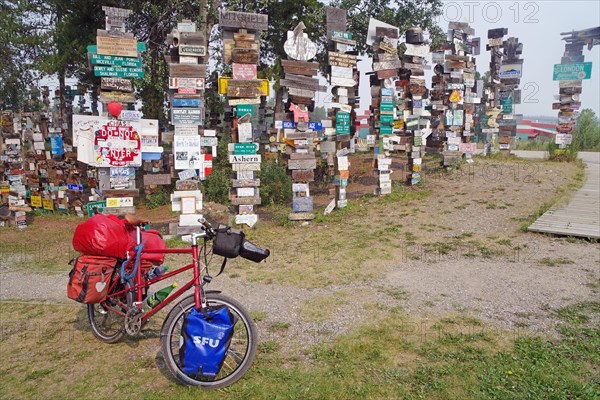 Various traffic and place signs face a bicycle loaded with luggage