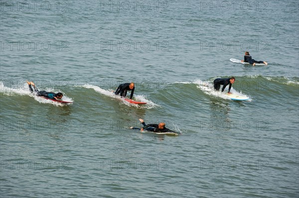 Surfers in wetsuits riding wave on surfboards as it breaks at sea