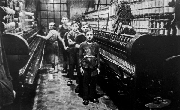 Old black and white archival photograph showing female worker and child labourers posing in spinning mill in the early twentieth century