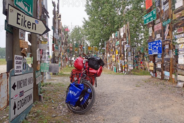 Various traffic and place signs face a bicycle loaded with luggage