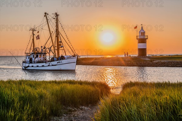 Crab cutter with the Kleiner Preusse lighthouse at the Sielhafen harbour at sunset