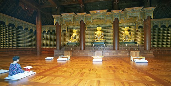 Korean woman praying at the golden Buddha statues in the temple