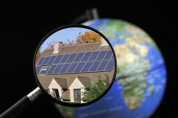 Photovoltaic solar panels on roof of house seen through magnifying glass held against illuminated terrestrial globe