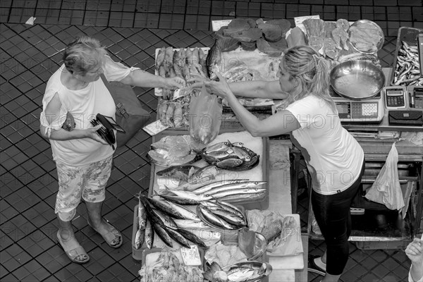 Black and white bird's eye view photo of a stall full of fish with the seller and a buyer