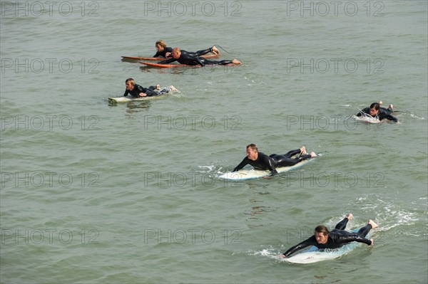 Surfers in wetsuits lying flat on their surfboards in the sea
