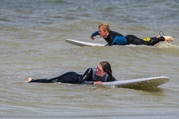 Female surfer in wetsuit lying and waiting on her surfboard for a big wave