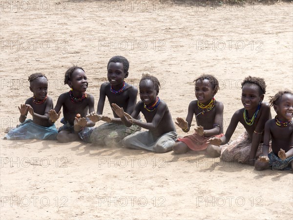 Singing happy children sitting on sandy ground