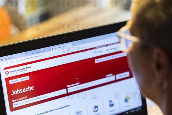 Woman with glasses looking for a job sits at home in front of her notebook and checks the internet site of the Federal Employment Agency for job offers