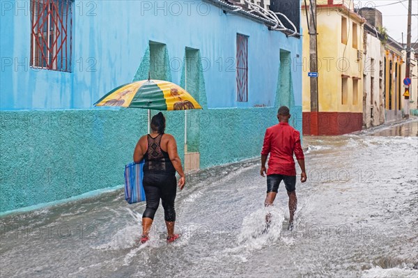 Cubans with umbrellas walking in flooded street during torrential rain in the city Santiago de Cuba on the island Cuba