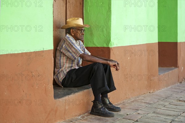 Portrait of old Cuban man sitting in front of pastel coloured house front in the streets of Trinidad