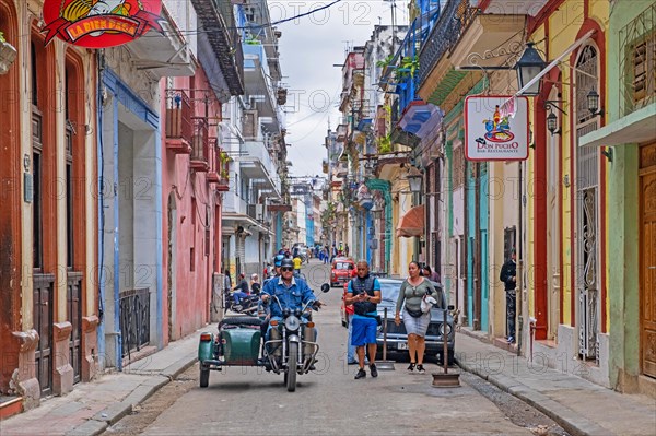 Cubans and motorcycle with sidecar in narrow street with bars and restaurants in the colonial city centre Old Havana