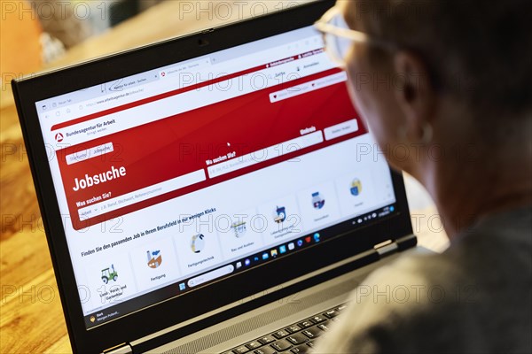 Woman with glasses looking for a job sits at home in front of her notebook and checks the internet site of the Federal Employment Agency for job offers