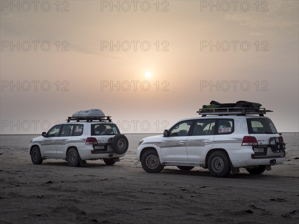 Tourists in off-road vehicles driving on salt desert at sunrise