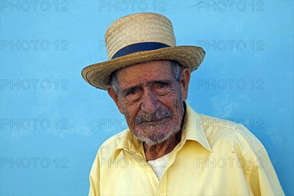 Portrait of old Cuban man posing in front of pastel coloured wall in the streets of Trinidad