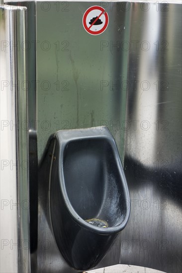 Public stainless steel urinal with sign prohibiting people to crap