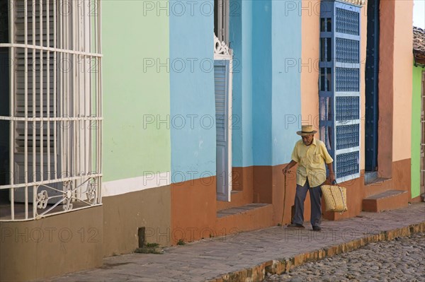 Old Cuban man walking along pastel coloured houses with barrotes and grilles in Trinidad