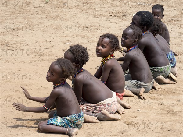 Singing happy children sitting on sandy ground