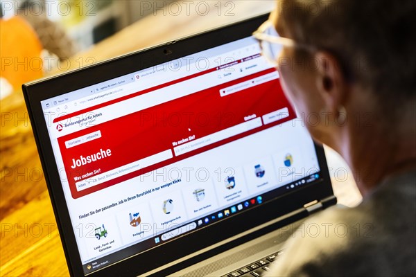 Woman with glasses looking for a job sits at home in front of her notebook and checks the internet site of the Federal Employment Agency for job offers