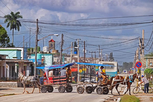 Horse-drawn carriage with passengers and horse with cart crossing road in the town Jatibonico