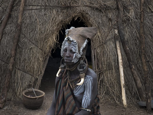 Woman from the Mursi tribe with headdress and face painting in front of her hut