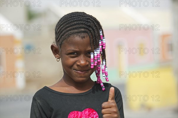 Creole girl with braided hair decorated with colourful beads showing thumbs up on the island Boa Vista