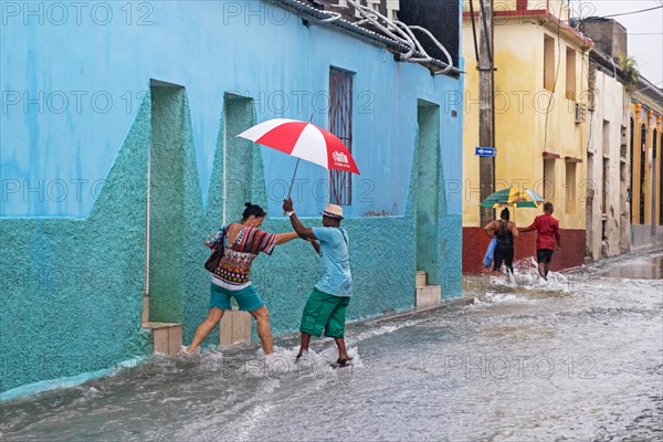 Cubans with umbrellas walking in flooded street during torrential rain in the city Santiago de Cuba on the island Cuba