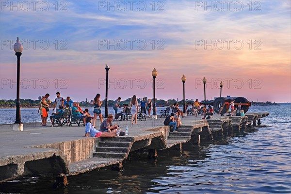 Cubans and tourists sitting on the concrete Muelle Real