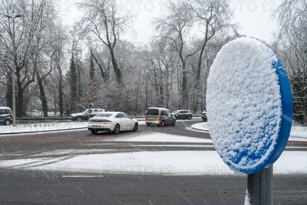 Cars on busy slippery intersection and road sign covered in snow during unexpected late sleet and snow shower in March 2023