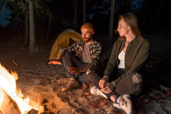 Couple warming up night by campfire