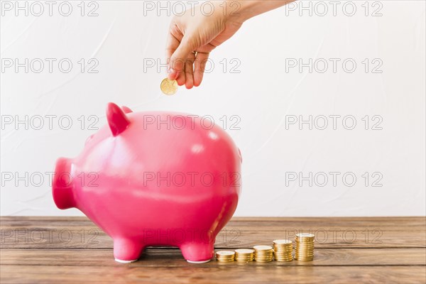 Human hand inserting coin pink piggybank