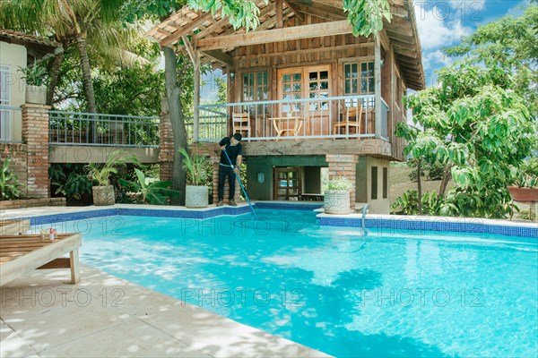 Man cleaning a beautiful swimming pool with suction hose. Swimming pool cleaning and maintenance service