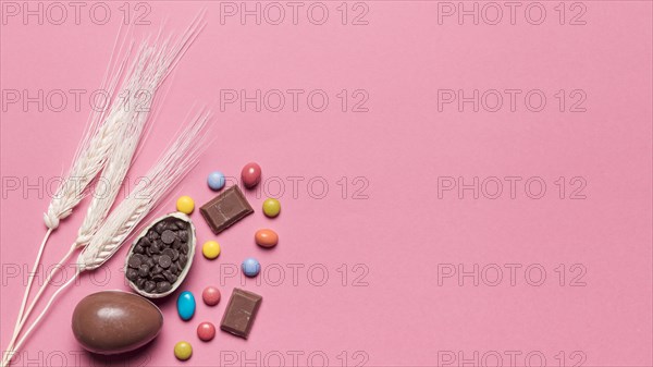 Three wheat ears with chocolate easter eggs gem candies pink background