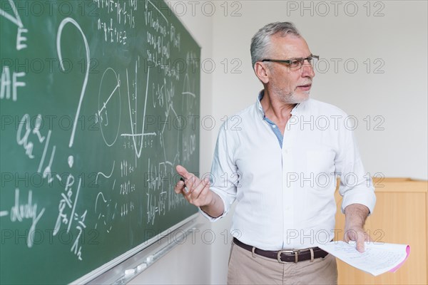 Aged math teacher explaining formula classroom