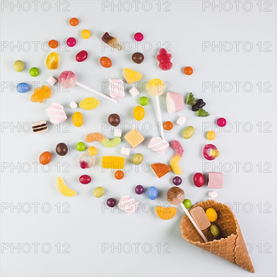 Elevated view various candies with ice cream waffle cone white background