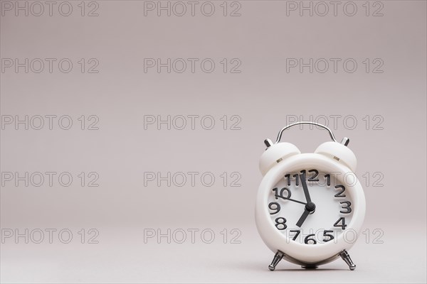 White miniature alarm clock against colored backdrop