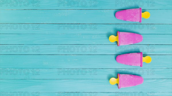 Bright pink frozen popsicles yellow sticks wooden background