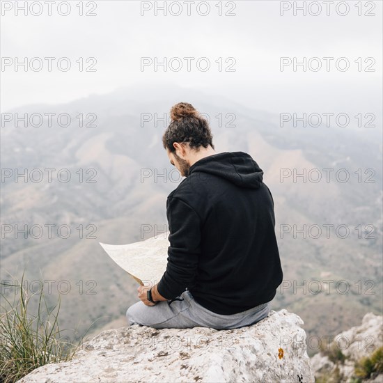 Male hiker sitting top rock looking map