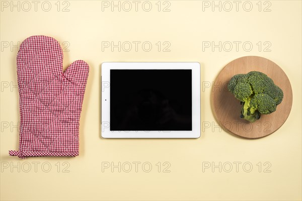 Mitt oven glove digital tablet broccoli wooden tray against beige background
