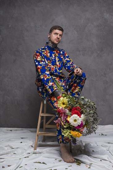 Thoughtful young man sitting wooden small ladder holding flower bouquet hand