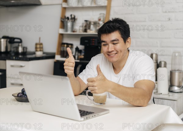 Man home during pandemic showing thumbs up during video call laptop