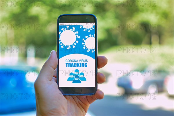 Tracking App concept for Corona virus with hand holding mobile phone with application design on screen in front of blurry outdoor background