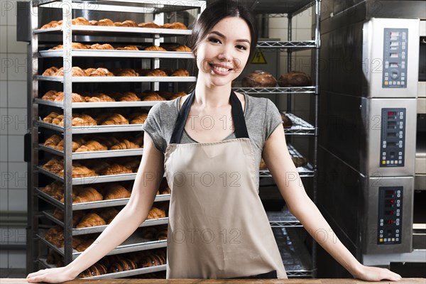 Portrait confident young female baker standing front baked croissant shelves