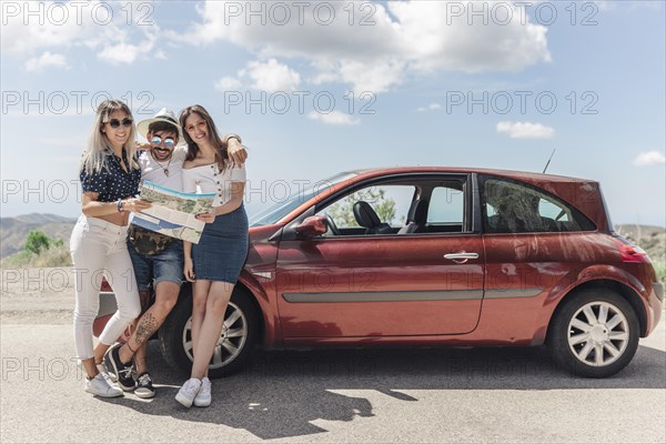 Three friends holding map standing near modern car road