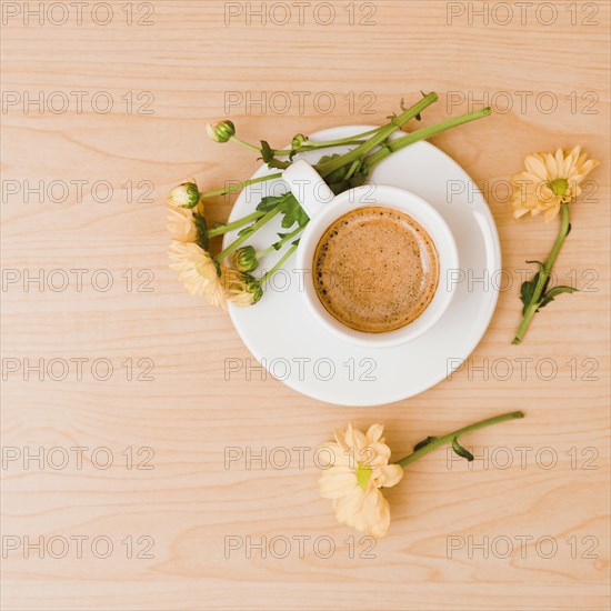 Overhead view coffee cup saucer with peach colored flowers wooden textured background